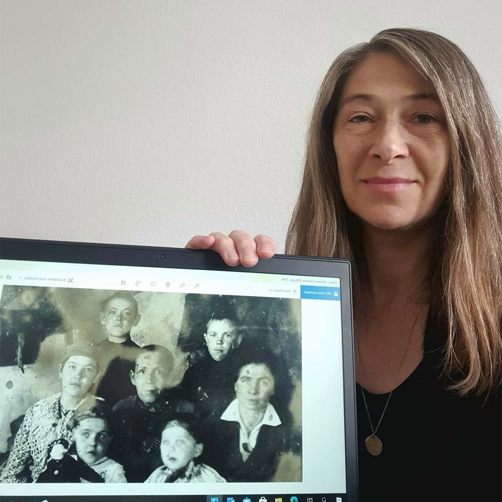 Natalie Kromm mit Foto ihrer Familie (Das Foto zeigt Maria Hölzer (Mitte) mit ihren minderjährigen Kindern 1943 in der Verbannung in Katenis. Von links oben: Sohn Eduard, Sohn Arnhold, Tochter Erna, Tochter Emma, Walter und Maria (Familie des Sohnes Heinrich)).